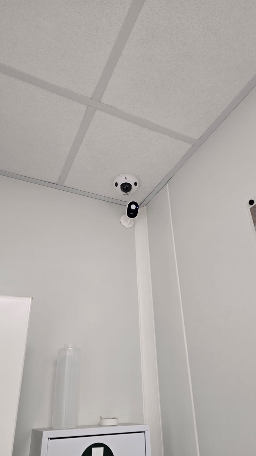 Technicien installant une caméra de sécurité dôme au plafond tout en gérant le système de maison intelligente avec un smartphone affichant un code de verrouillage.