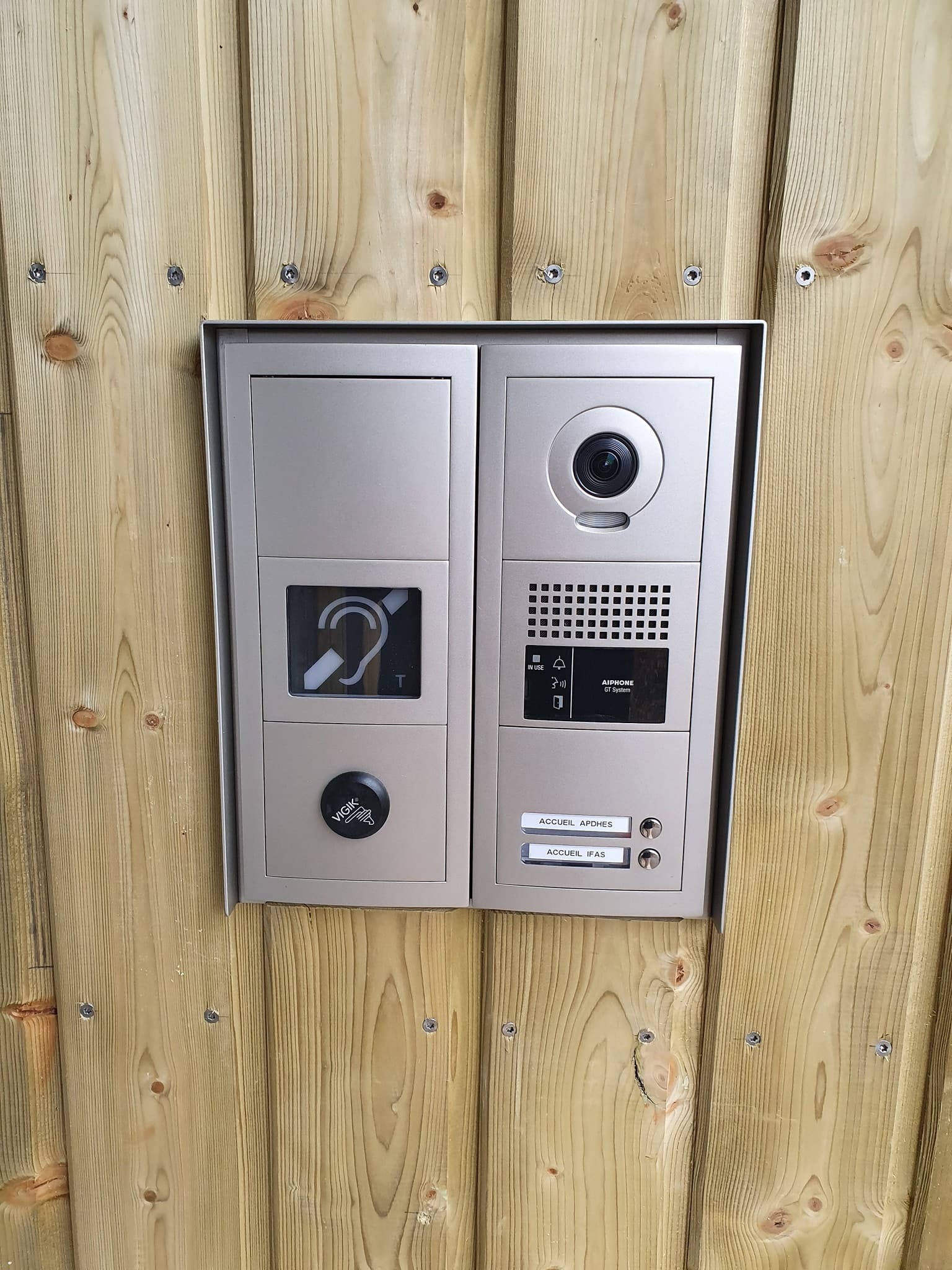 Interphone vidéo et sonnette extérieure VIGIK sur bardage bois clair, avec pictogramme malentendant et boutons "ACCUEIL APDHES" et "ACCUEIL IFAS".