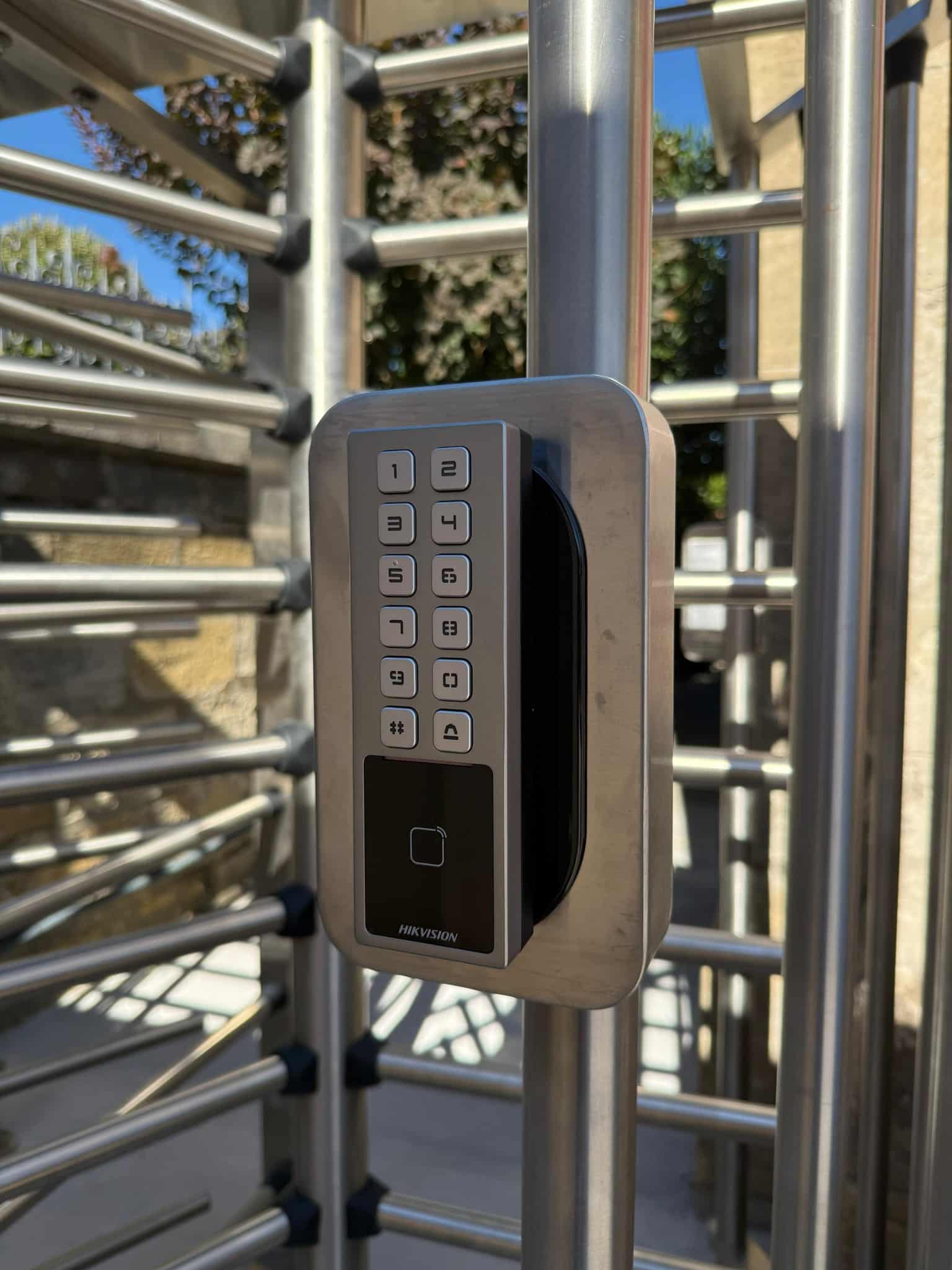 Lecteur d'accès HIKVISION avec clavier numérique et scanner biométrique fixé sur le poteau d'un tourniquet en acier inoxydable.