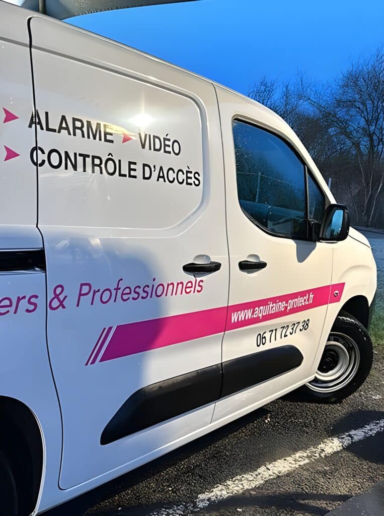 Partie latérale d'un utilitaire blanc avec lettrage rose et noir : ALARME VIDÉO CONTRÔLE D'ACCÈS, aquitaine-protect.fr, 06 71 72 37 38.